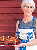 Lächelnde ältere Frau hält Tablett mit Muffins