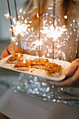 Hands holding dessert with igniting sparklers