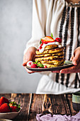 Woman holding a plate with pancakes with fruit, raspberries, pomegranate mint and yoghurt