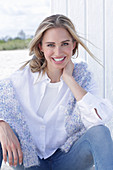 A long-haired blonde woman wearing a white shirt blouse and jeans with a jumper over her shoulders