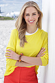 A long-haired blonde woman wearing a yellow top and red trousers