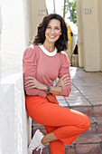 An older brunette woman wearing a pink top and orange trousers