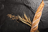 Baguette next to wheat ears and grains