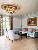 Silbergraue Polstergarnitur, Mahagonitisch und vergoldete Deckenrosette im Wohnzimmer