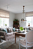 Upholstered sofa with cushions, antique corner cupboard, old wooden table, above it chandelier in the living room