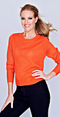 A long-haired woman wearing an orange jumper and black trousers