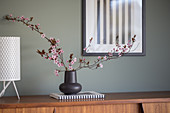 Sprigs of cherry plum blossom in a black vase on a sideboard