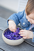 A girl reaching into a bowl of violet flowers