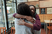 Happy mother and daughter hugging in cafe