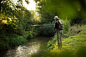 Man with backpack fly fishing at riverbank