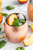 Moscow mule garnished with peach slice and basil leaves