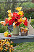 Osterstrauß aus roten und orangefarbenen Tulpen, Osterhase aus Holz und Ostereier im Drahtkorb