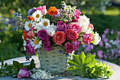 Bouquet of roses, daisies, lilacs, borage, and wood avens in a basket, lady's mantle leaves