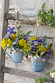 Small spring bouquets with columbines, milkweed, comfrey, knapweed, and speedwell in mugs hung on wooden ladders