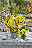 Easter bouquet of flowering branches of forsythia, decorated with Easter bunny ornaments, and Easter eggs