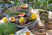 Small Easter picnic in the garden: boiled Easter eggs with Keta caviar, bread, chives, dandelion flowers, small bowls with cress and glasses