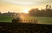 Pflügen eines Feldes bei Sonnenuntergang mit einem Traktor