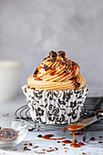 A coffee cupcake on a wire rack with caramel dripping off a knife alongside it