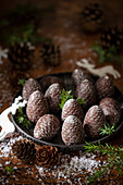 Pine cone shaped chocolates on a metal plate surrounded by fir springs and real pine cones