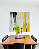 Wooden table with black leather chairs in front of artwork in dining area