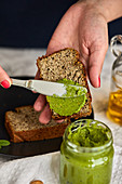 Spreading homemade basil and arugula pesto in a jar on a piece of bread