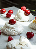 Individual meringues topped with raspberries, whipped cream and cherries