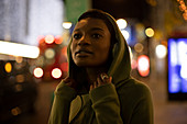 Young woman in hoodie on city sidewalk at night
