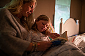 Mother reading bedtime story to daughter in bed