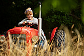 Happy woman driving tractor in orchard
