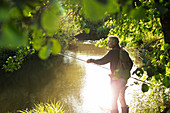 Man fly fishing at sunny summer riverbank