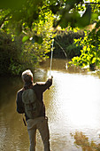 Man with backpack casting fly fishing pole at river