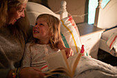 Happy mother and daughter reading bedtime story in bed