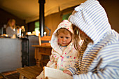 Sisters in hooded bathrobes reading book in cabin