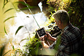 Man with digital tablet fly fishing at sunny riverbank