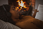 Woman with headphones reading book at fireplace