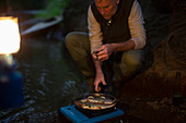 Man cooking fresh caught fish on camping stove at night