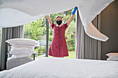 Female hotel maid in face mask making bed in hotel room