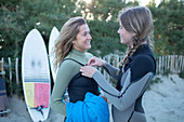Happy young women friends putting on wet suits on beach