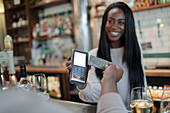 Customer paying female bartender with smart card in bar