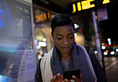 Young woman using smartphone at urban bus stop at night