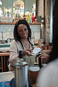 Friendly female bartender giving bill to customer in bar