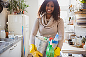 Smiling woman with cleaning supplies in kitchen