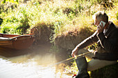 Man fly fishing and talking on smartphone at sunny river