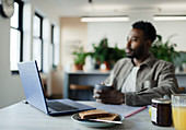 Thoughtful businessman drinking coffee at laptop in office