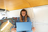 Happy young woman with headphones and laptop in camper van