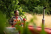 Happy man harvesting fresh red apples at tractor in orchard