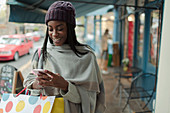 Young woman with shopping bag using smartphone on sidewalk