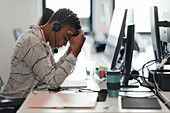 Tired businesswoman with head in hands at computer in office