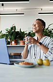 Happy businesswoman with coffee laughing at laptop in office