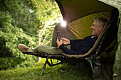 Man in camping lounge chair fishing and using digital tablet